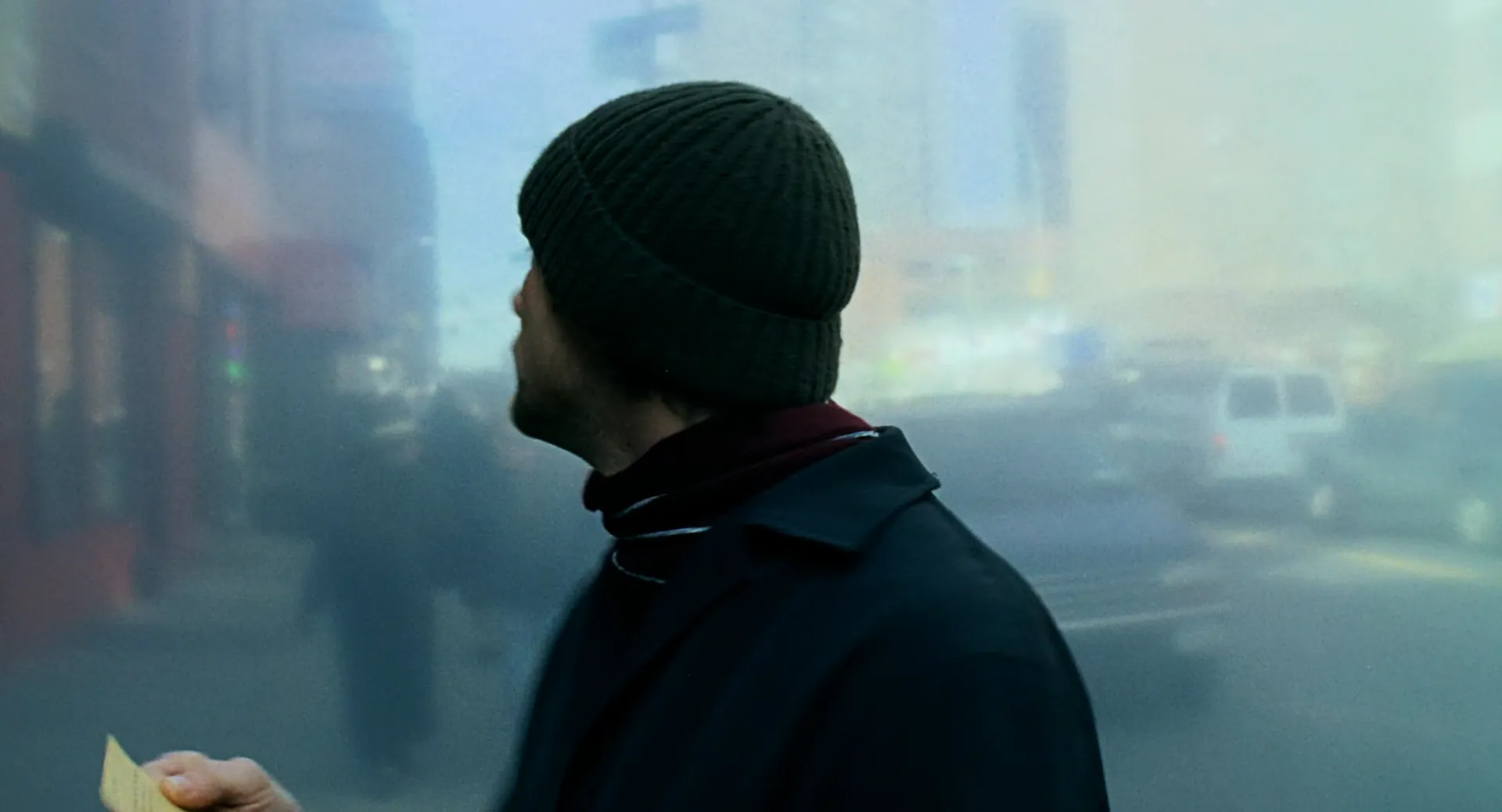 Eternal Sunshine of the Spotless Mind (2004) — a man in a dark coat and beanie in profile, the winter street behind him compressed into a soft, colorless wash