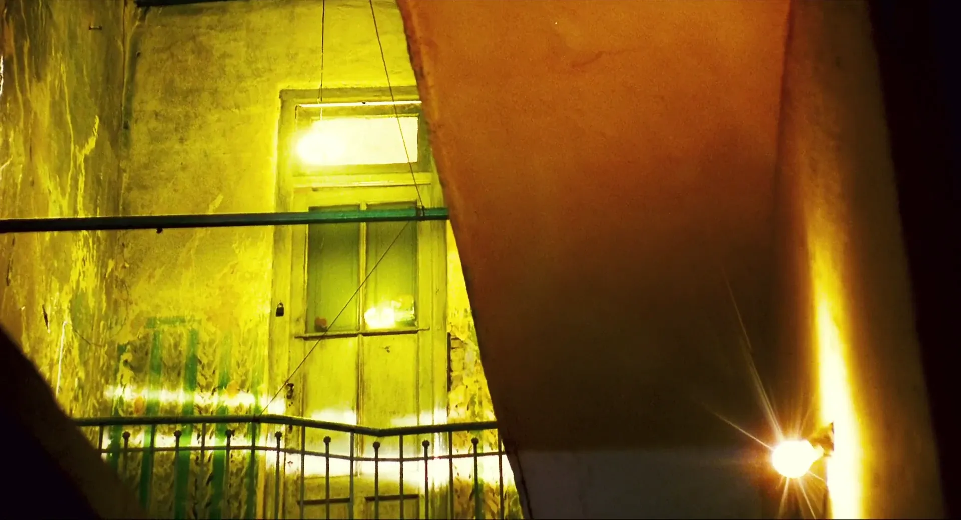 A decayed stairwell in Happy Together (1997) lit in acid green-yellow with a hard tungsten flare