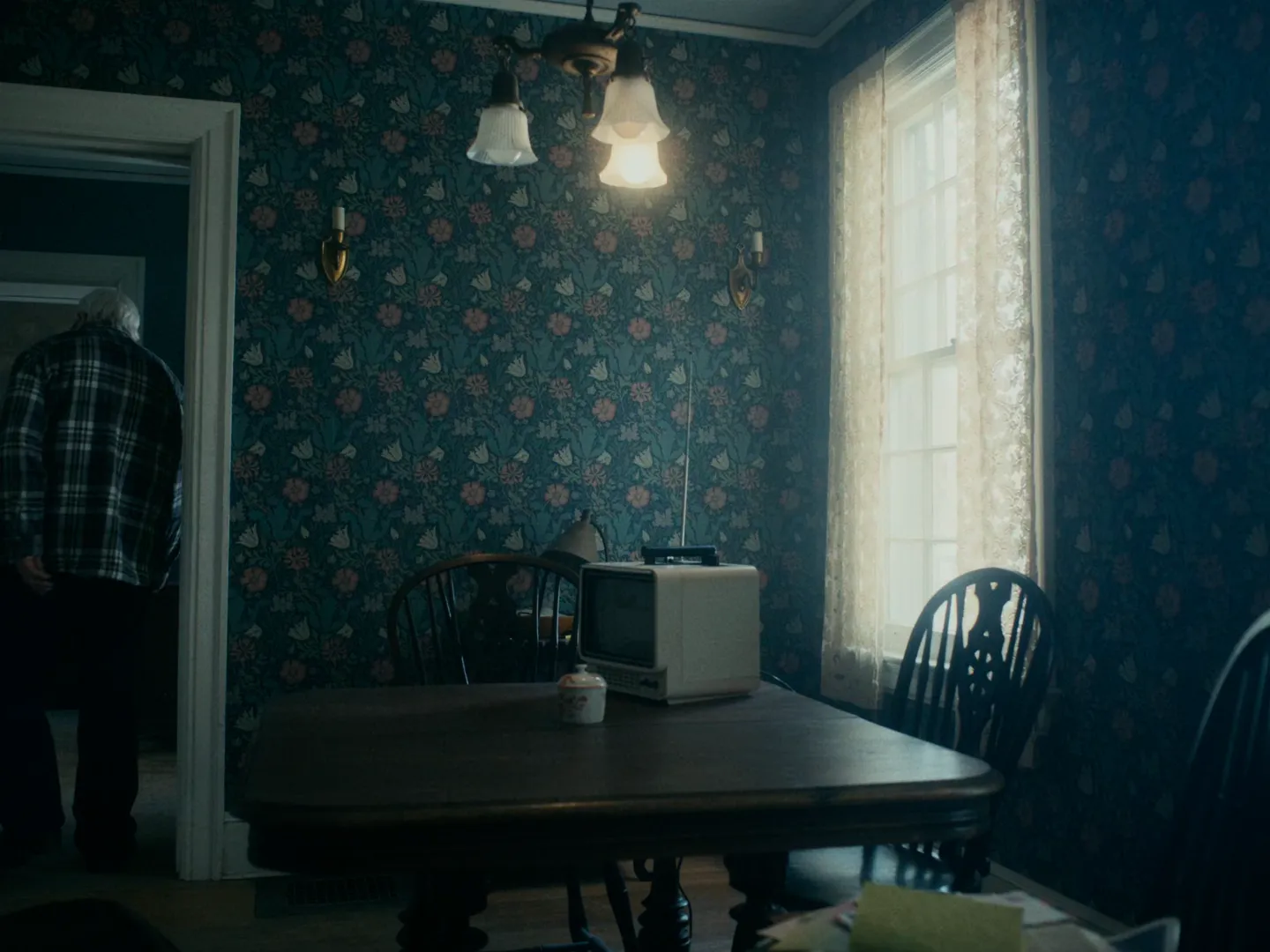 I'm Thinking of Ending Things (2020) — an ordinary domestic interior under a single practical fixture, Żal shaping a room with only the light that was already in it