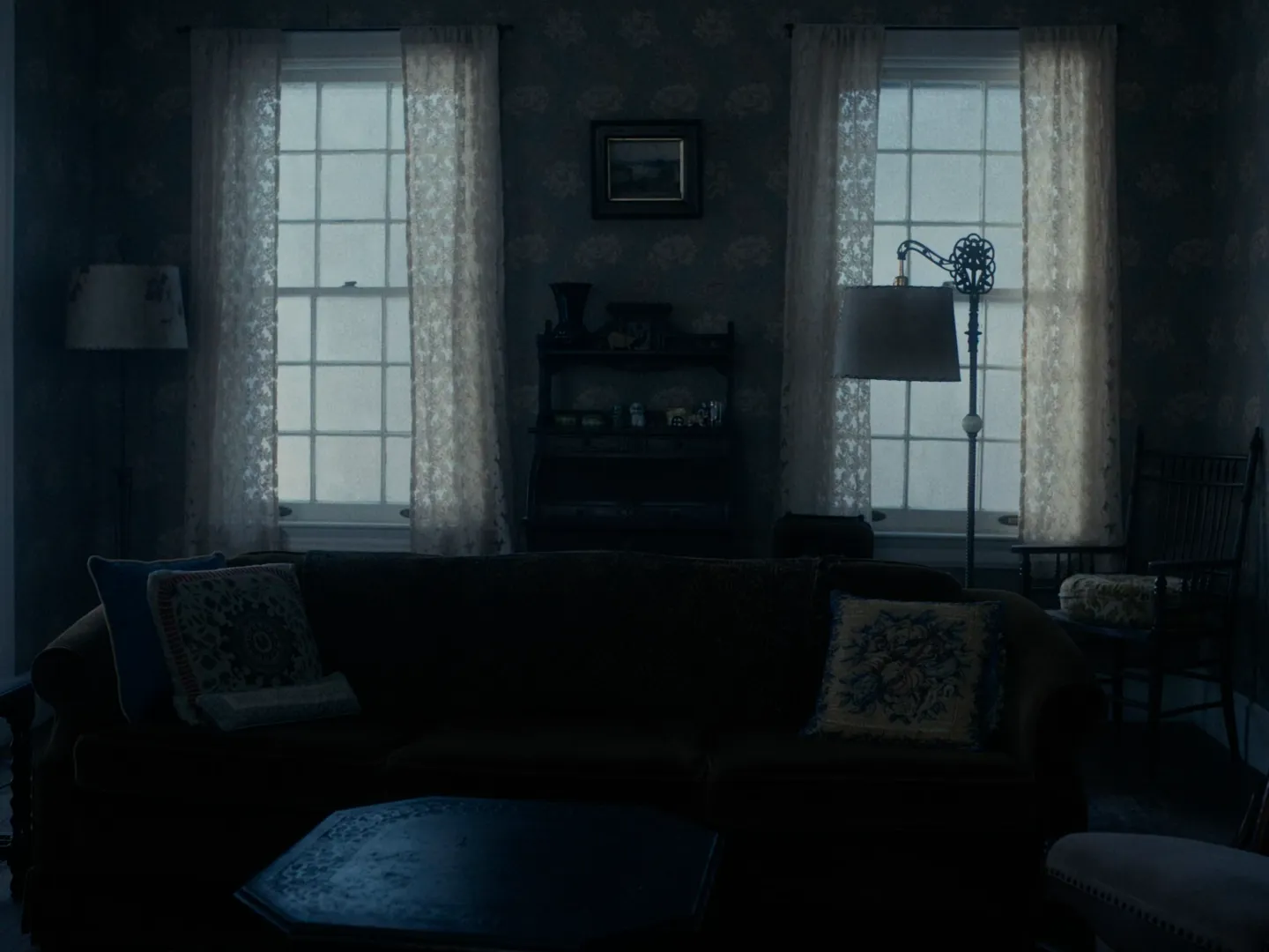 I'm Thinking of Ending Things (2020) — a living room lit by two curtained windows with practical lamps in the corners