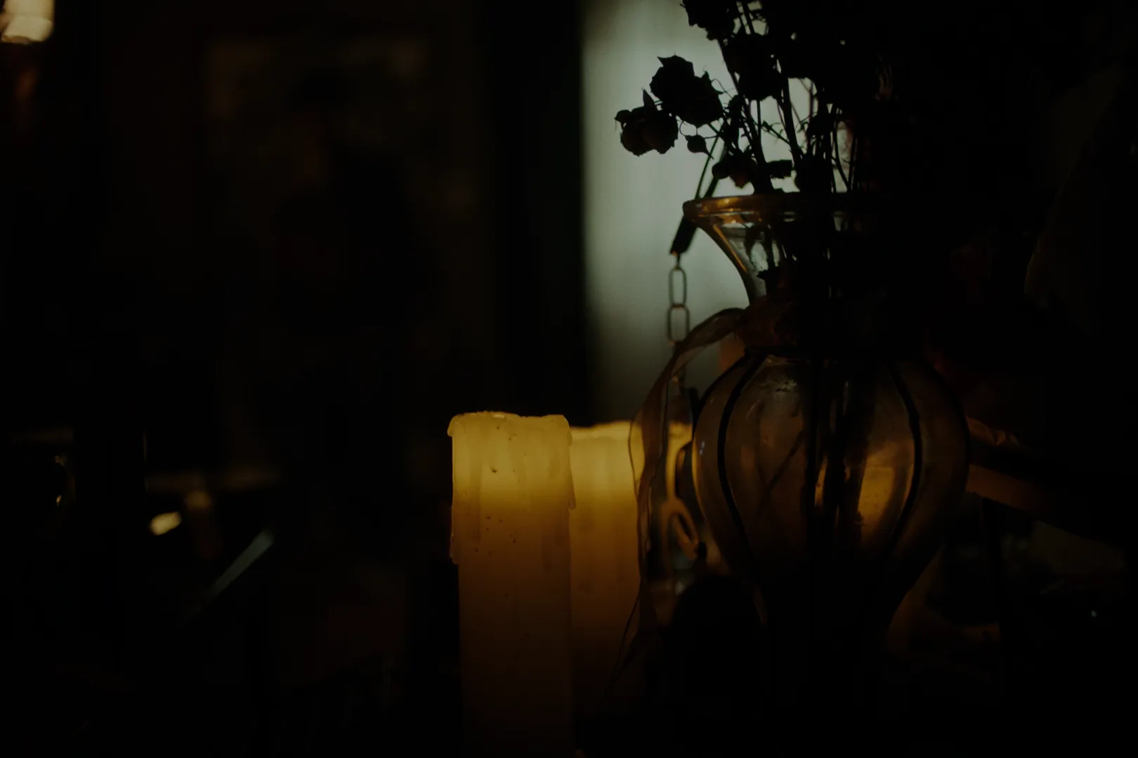 Obsession (2026) — a single guttering candle and a glass vase carrying the entire warm, hushed temperature of a scene.