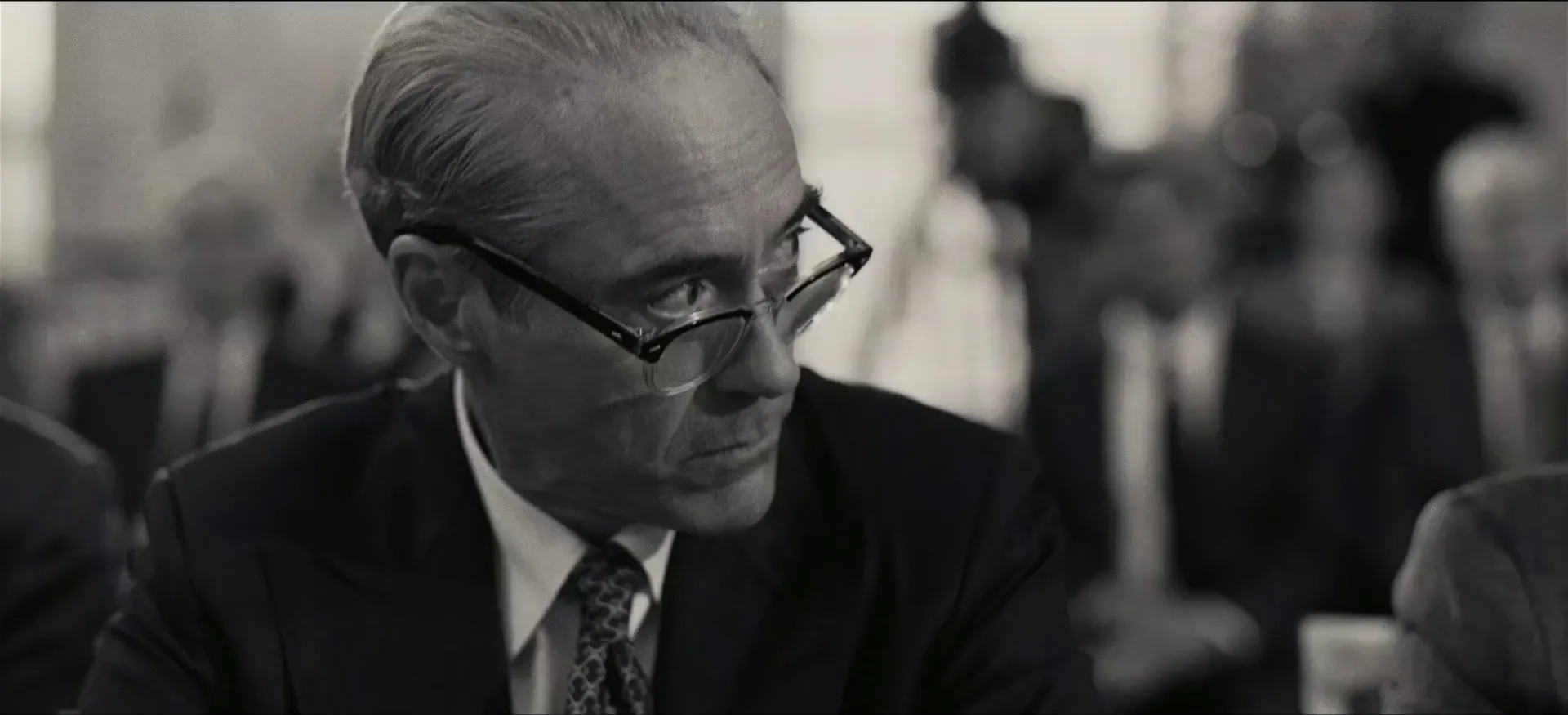 Black-and-white close-up on a bespectacled man at a hearing table, shallow focus, shot on the custom 65mm monochrome stock (Oppenheimer, 2023)