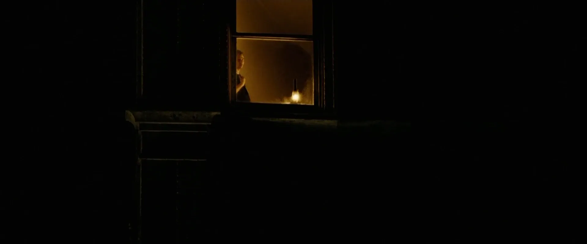 Illustrative frame β a figure at a night window with an oil lamp burning on the sill, the interior glowing off a single practical source (The Assassination of Jesse James by the Coward Robert Ford, 2007)