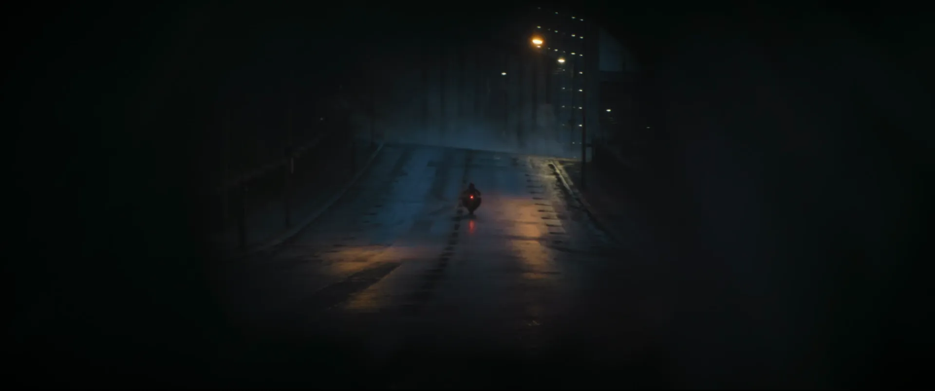 A lone motorcycle rider in a single pool of streetlight on a wet Gotham road, The Batman (2022)