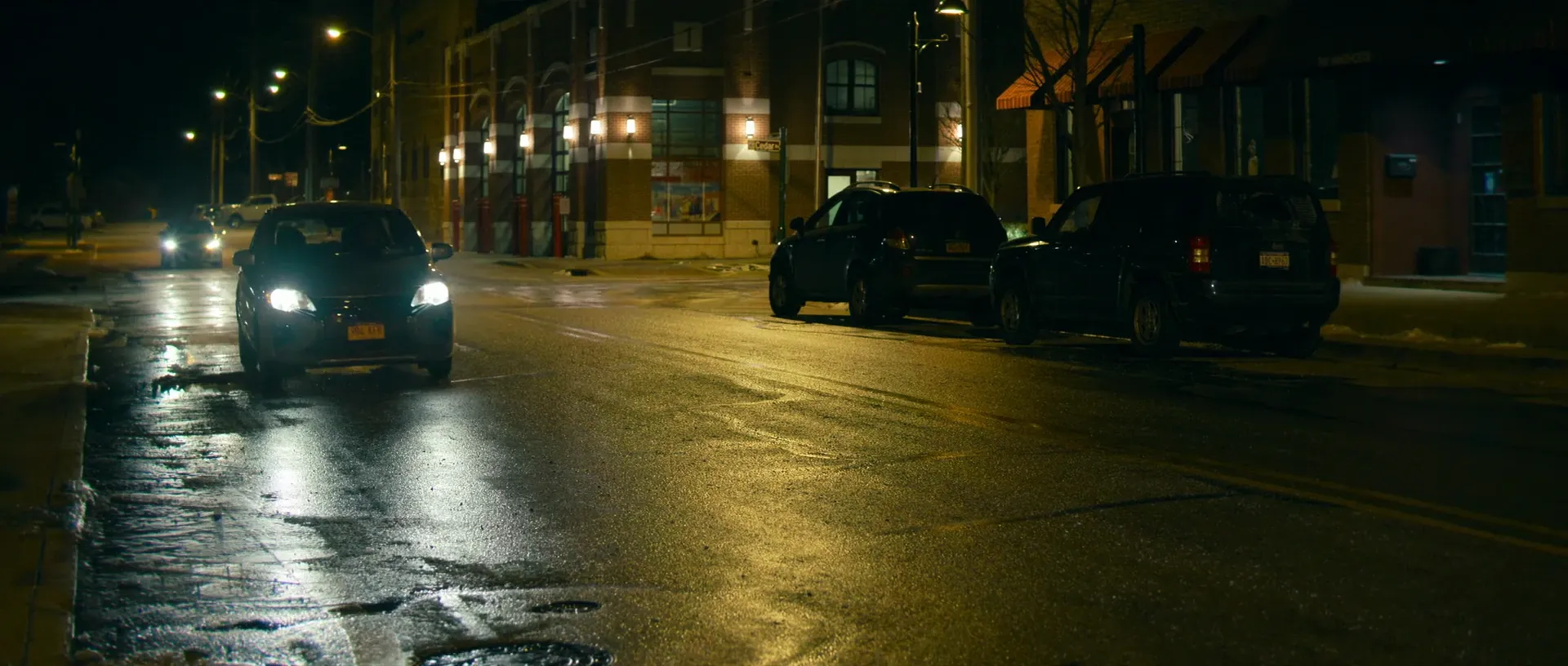The Killer (2023) — a night exterior: wet asphalt, working streetlights and headlights, and the shortest, most expensive hours on your schedule
