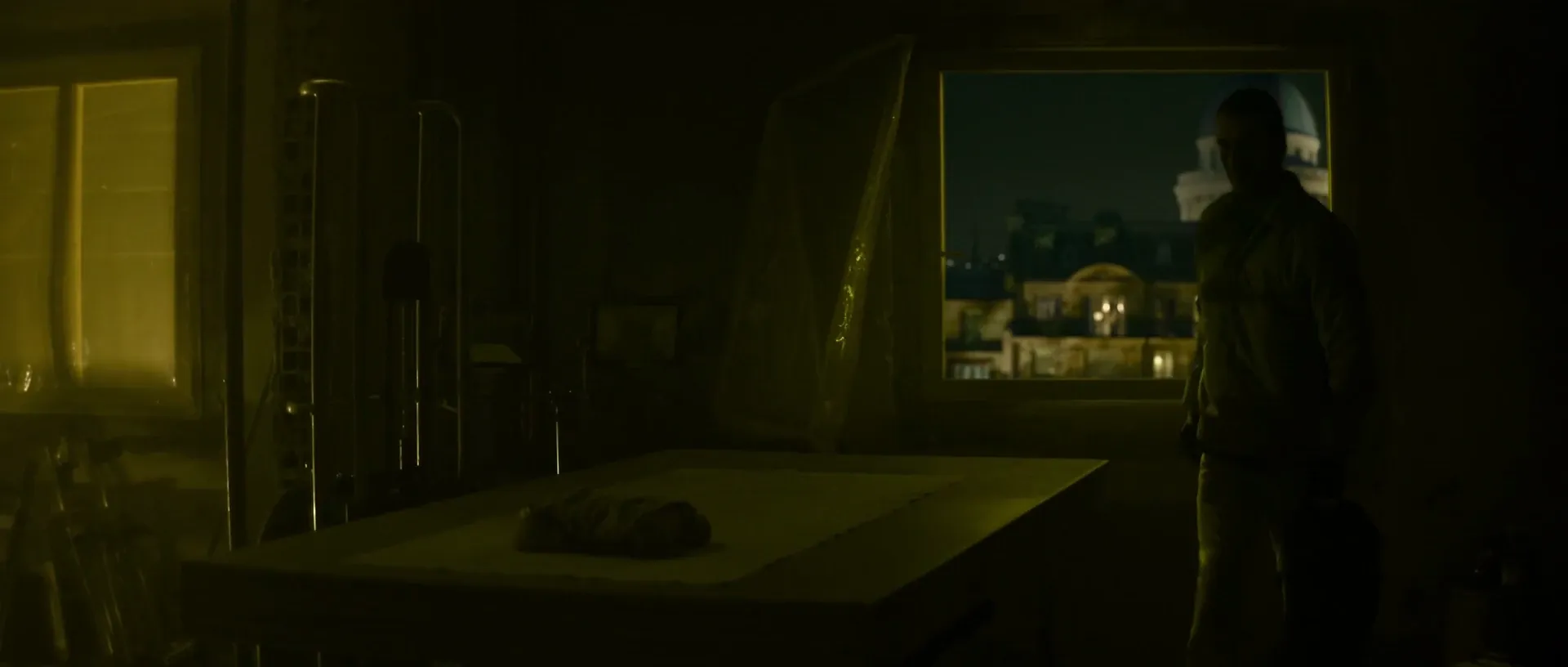The Killer (2023) — a dark interior lit only by a warm city window, the figure reduced to a silhouette