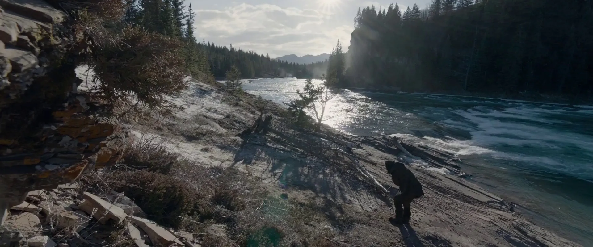 The Revenant (2015) β a wide spherical frame with a figure small on a riverbank, foreground rock, distant mountains and sun flare all held in deep focus