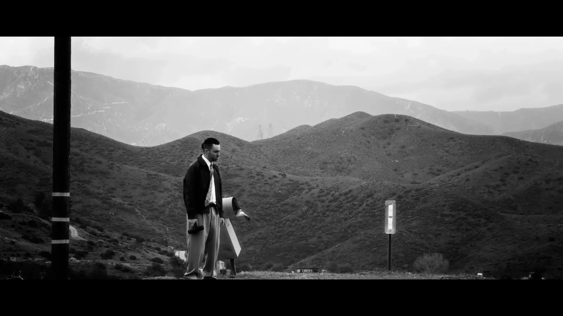 A lone figure in a suit standing small in a vast, sharp landscape of hills and distant mountains
